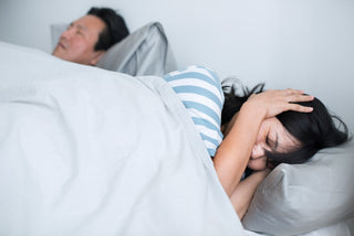 Woman covering ears in bed from snoring partner