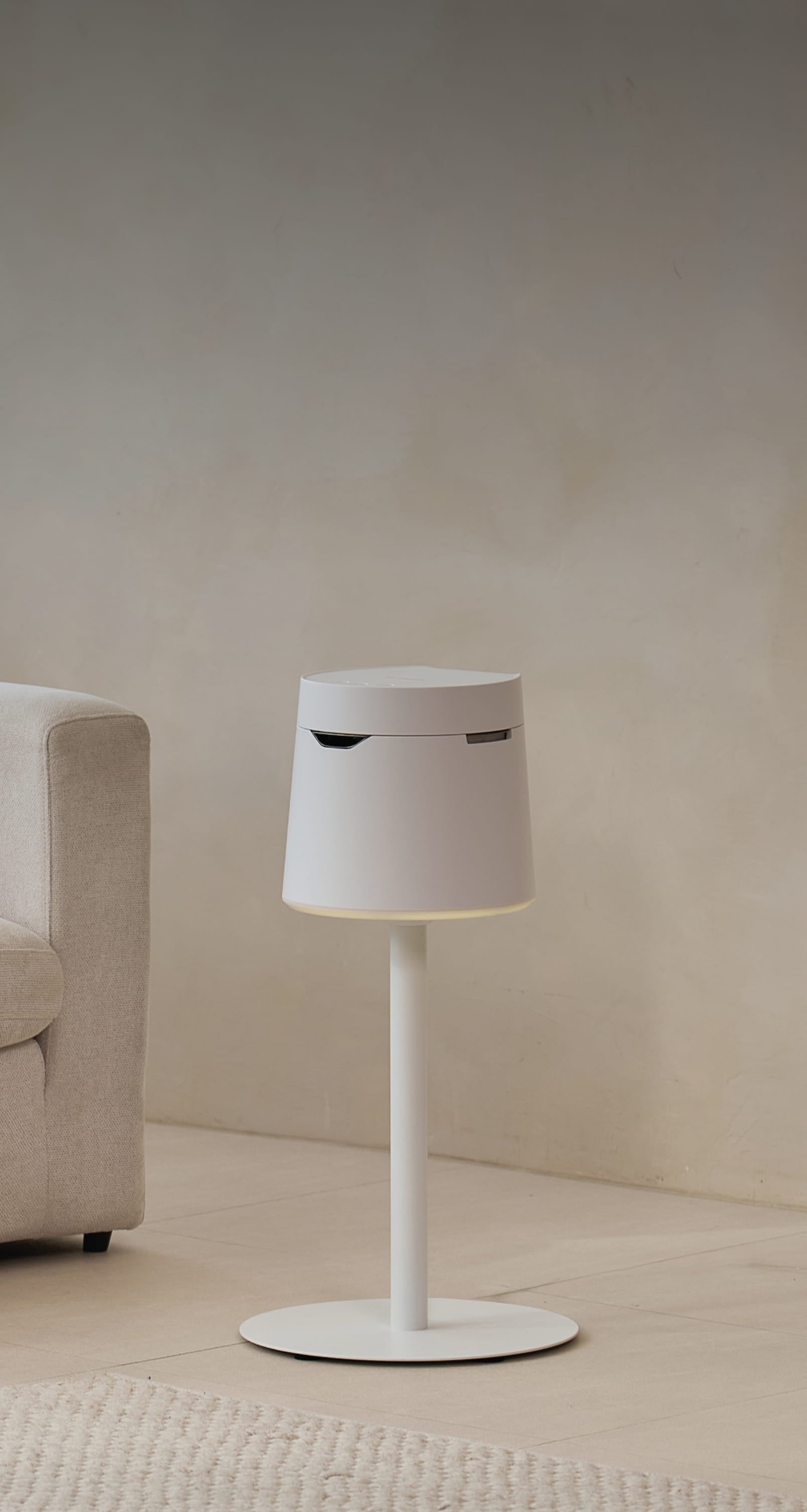 White Carepod humidifier with a cylindrical shape and a round base, next to a beige sofa
