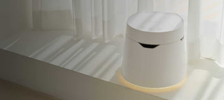 White air purifier with a glowing base, next to a window with sheer white curtains