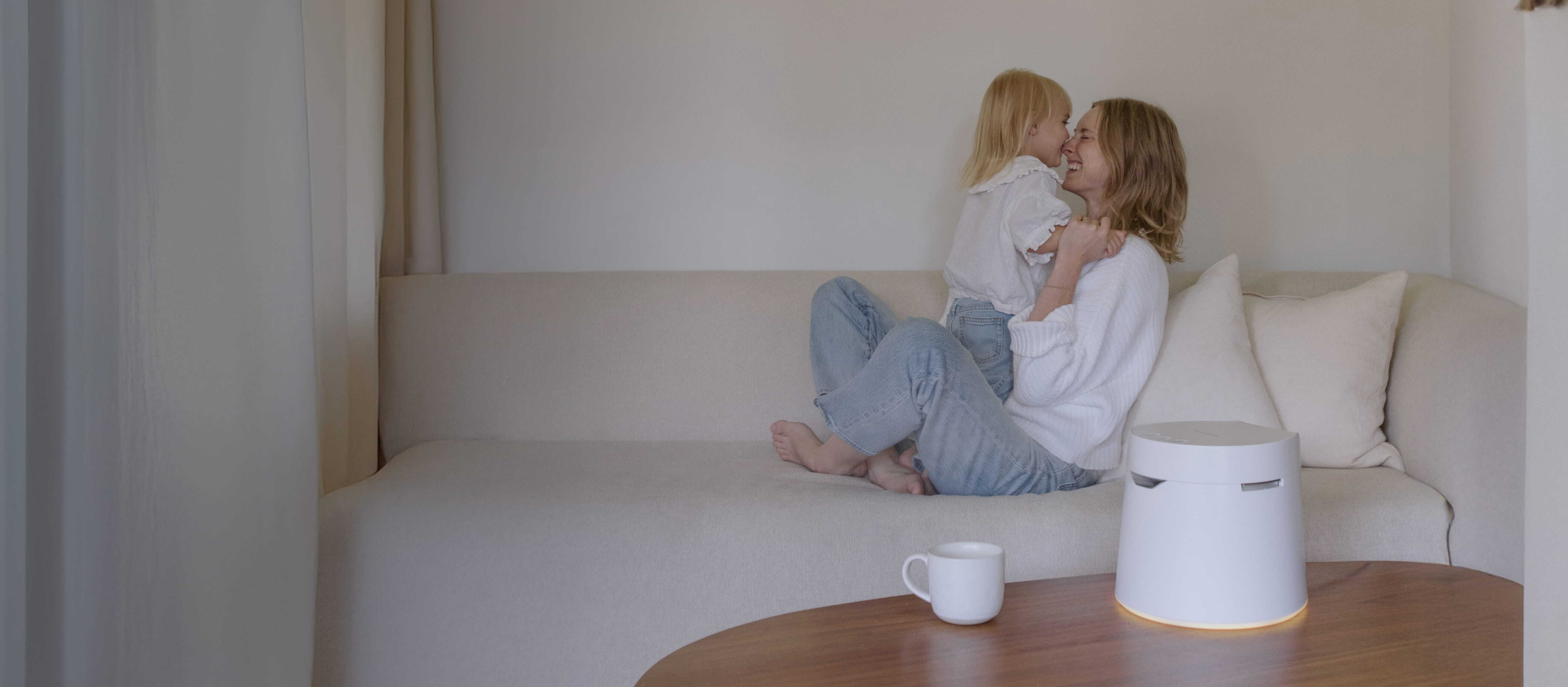 Mother and child on a sofa, with a white light and a white humidifier on a wooden table.