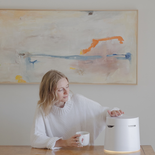 Woman sitting at a table touching a Carepod humidifier and holding a mug