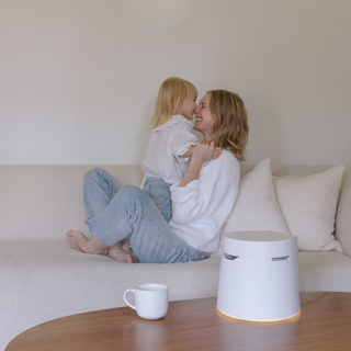 Mother and child playing on a couch beside a Carepod humidifier on a coffee table