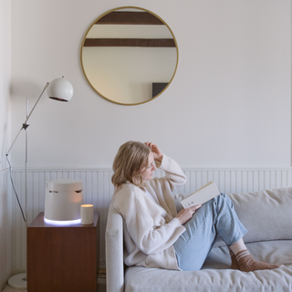 Woman reading a book on a sofa with a Carepod humidifier glowing on a side table nearby
